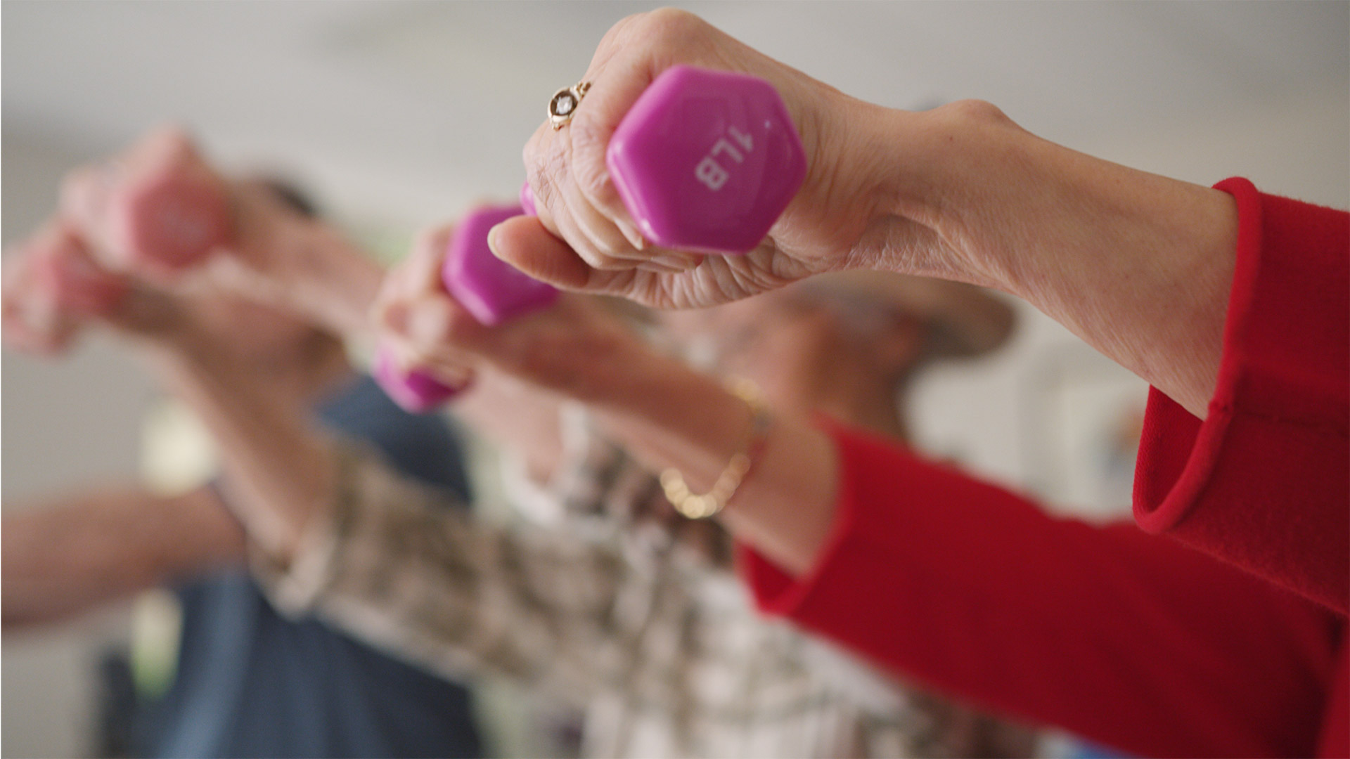Seniors lifting pink dumbbells at an assisted living facility.