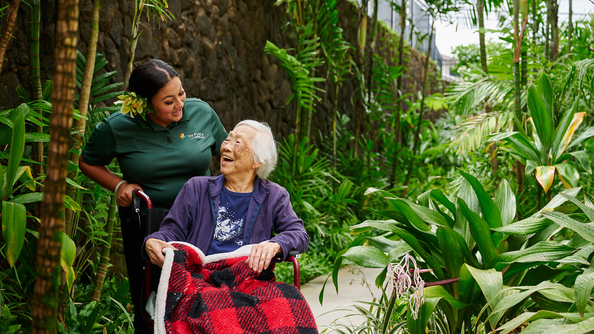 Staff member smiling and talking with a resident in a wheelchair during a garden walk.