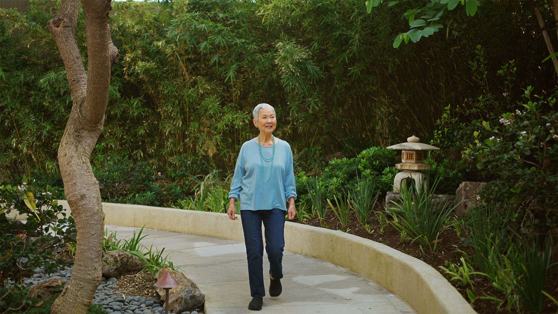 Resident walking through a lush zen garden at the plaza assisted living.