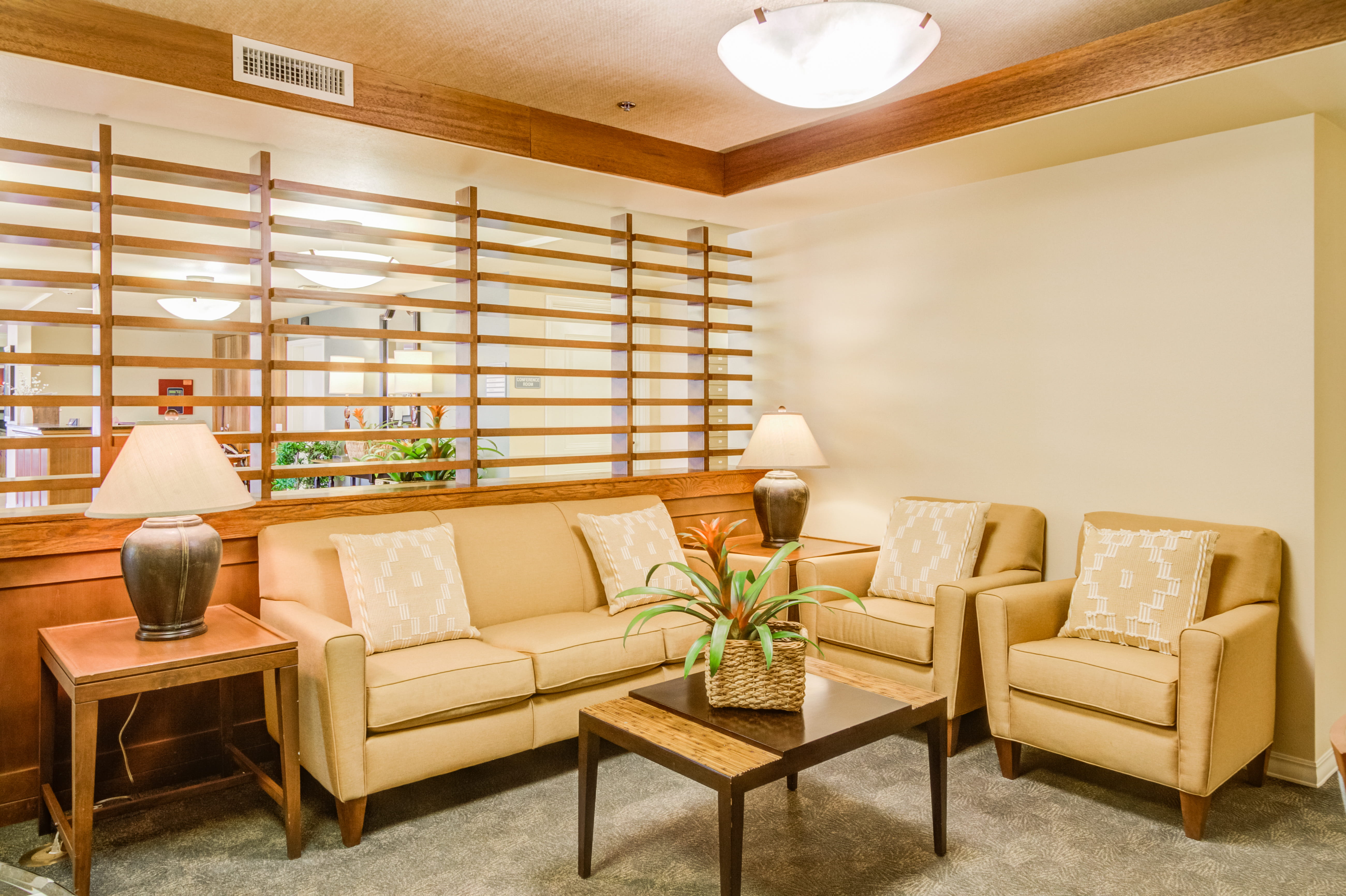Cozy sitting area with tan sofa and chairs at The Plaza Assisted Living Mililani.