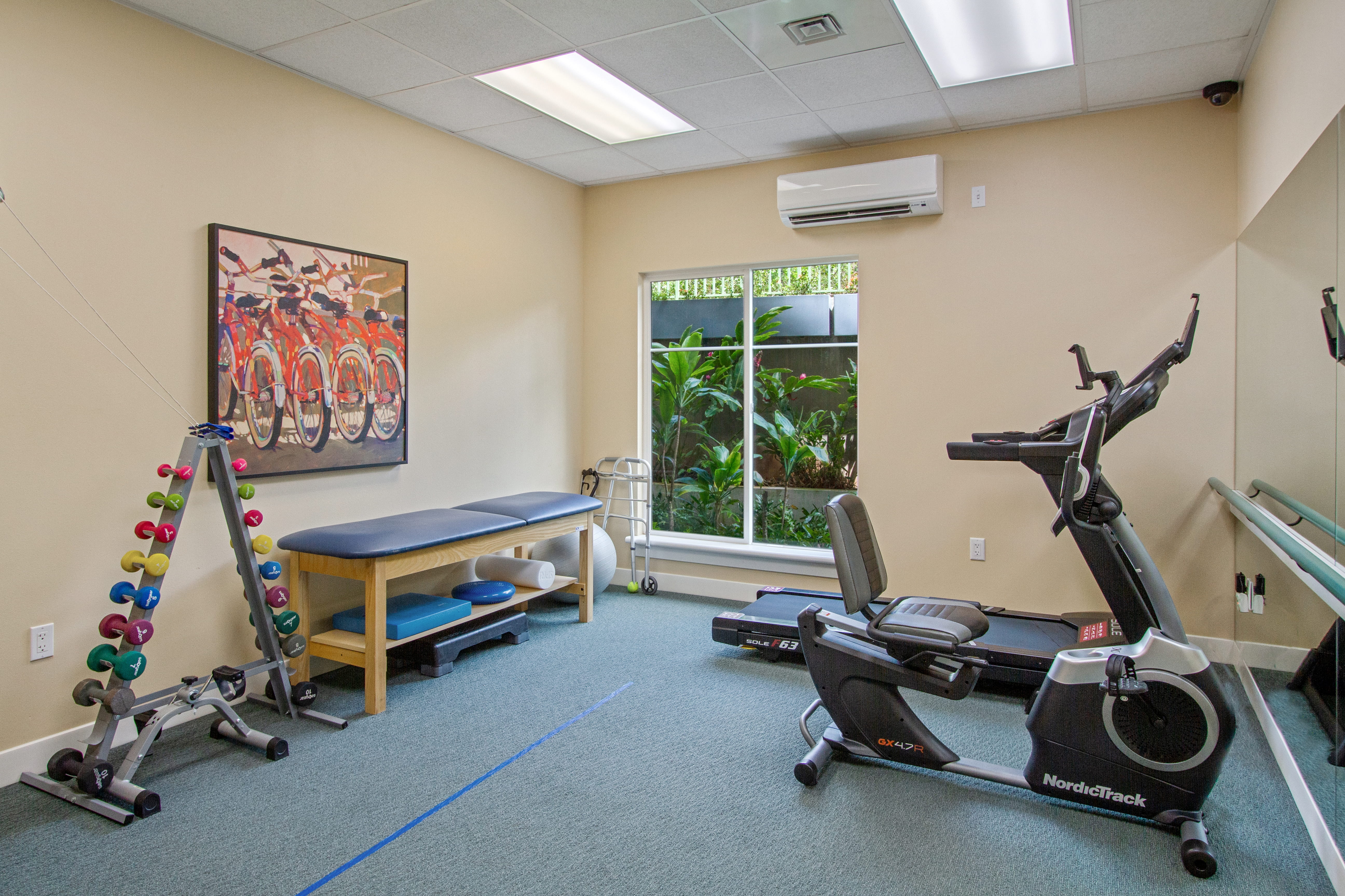 Fitness center at The Plaza Assisted Living Moanalua with exercise equipment and therapy bench.