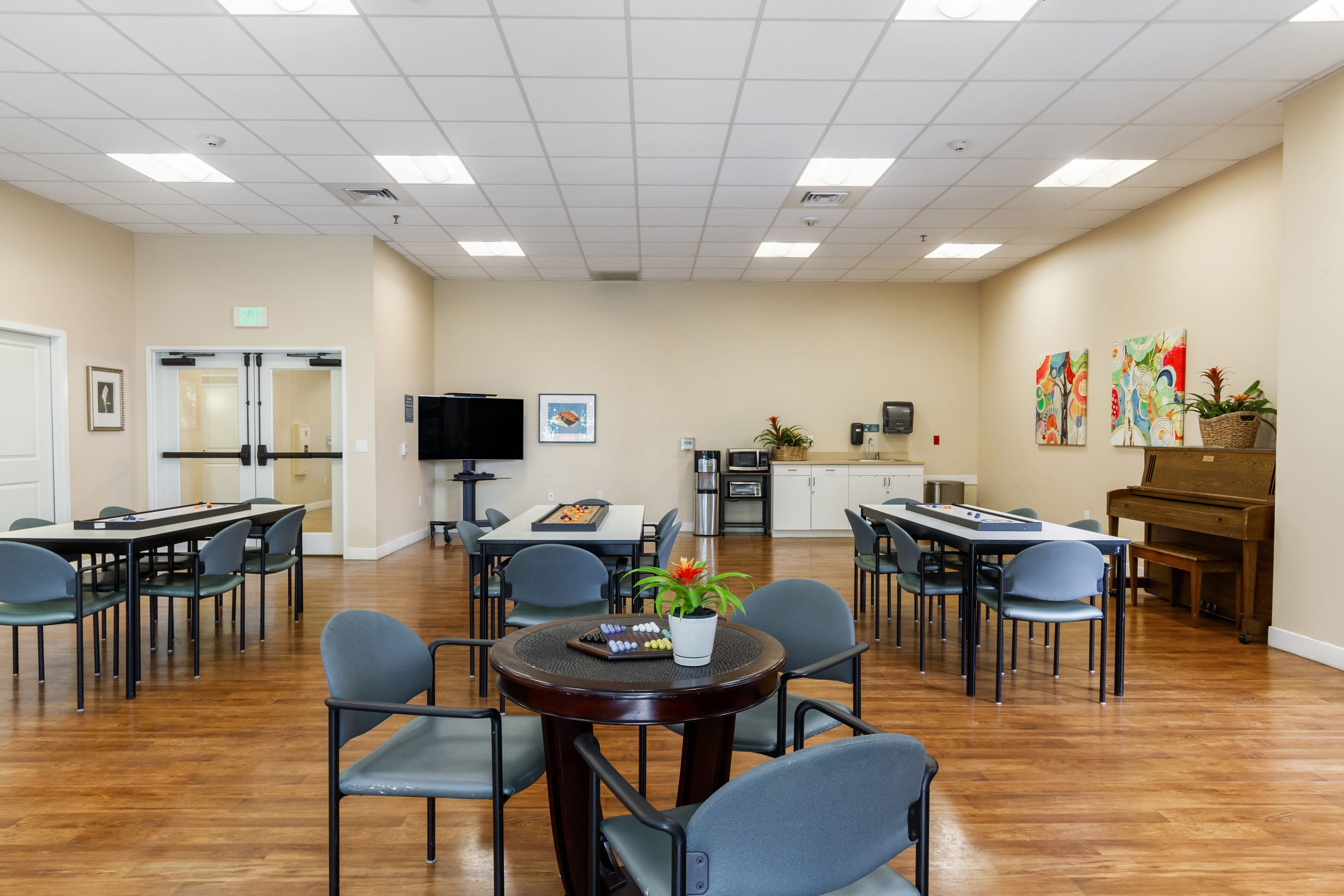 Activity room at The Plaza Assisted Living with game tables, a piano, and a TV.