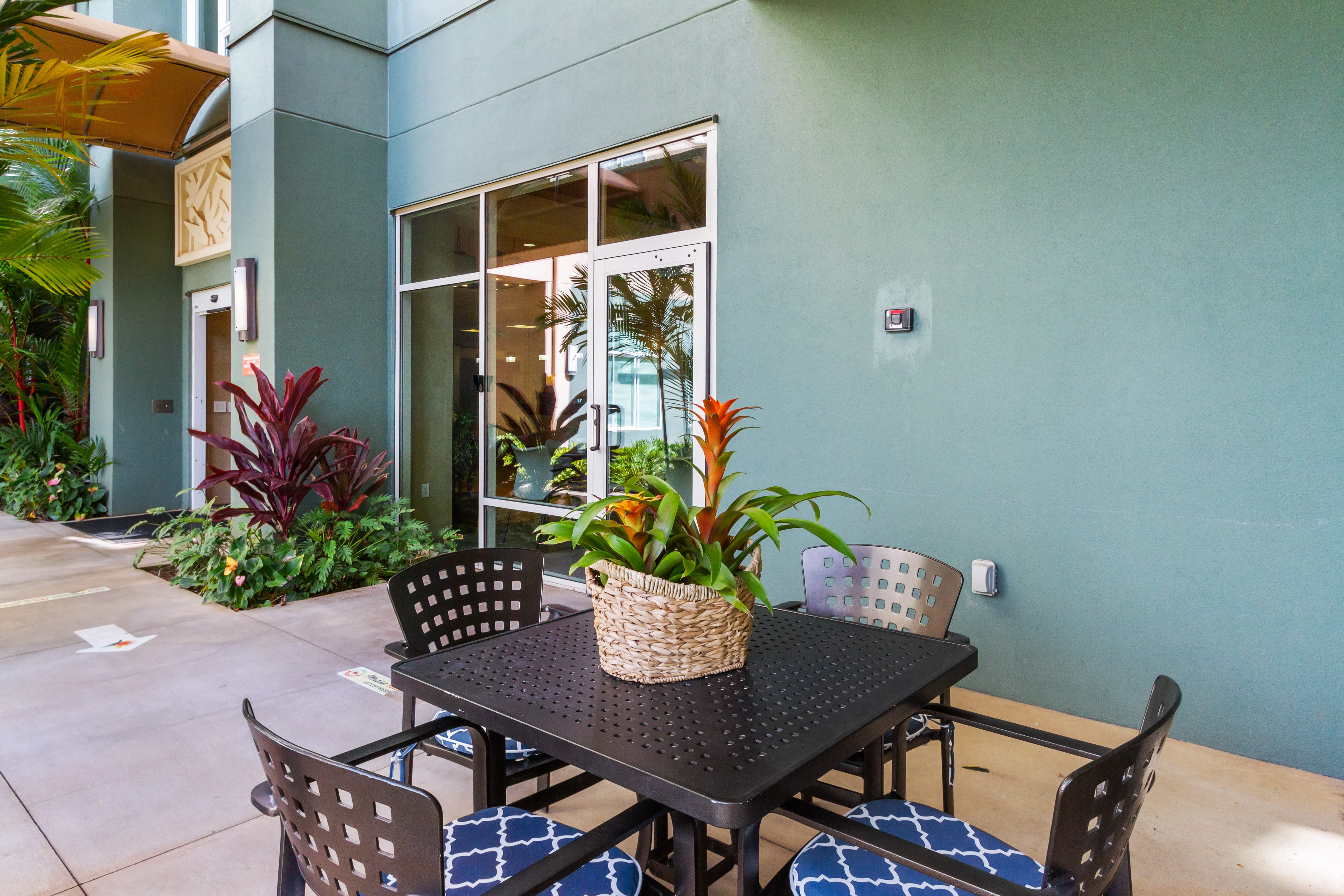 Outdoor dining table and chairs in a tropical courtyard at The Plaza Assisted Living.