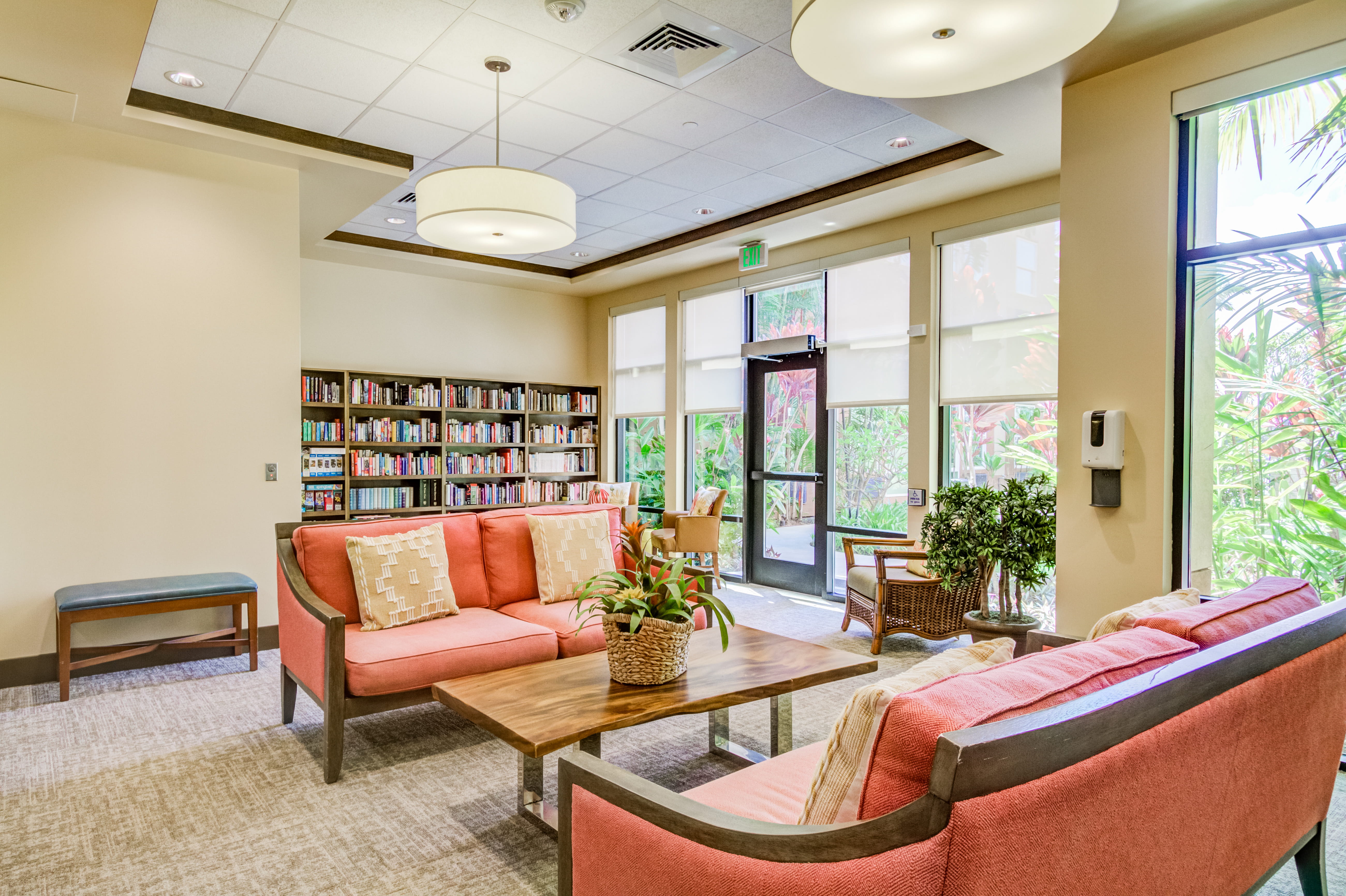 Social lounge with coral sofas and a resident library at The Plaza Assisted Living.