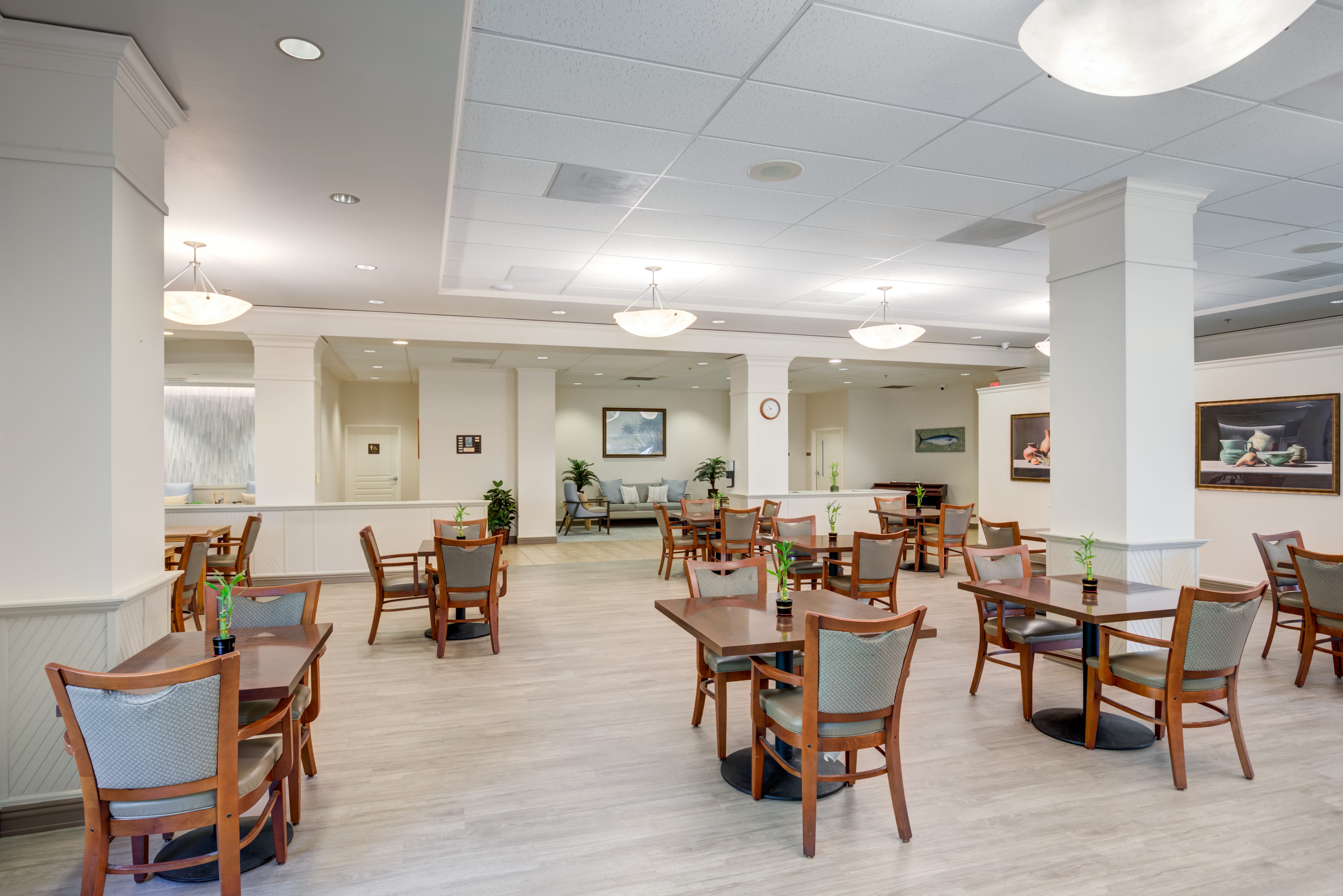 Spacious dining area with wooden tables and white columns at The Plaza Assisted Living.