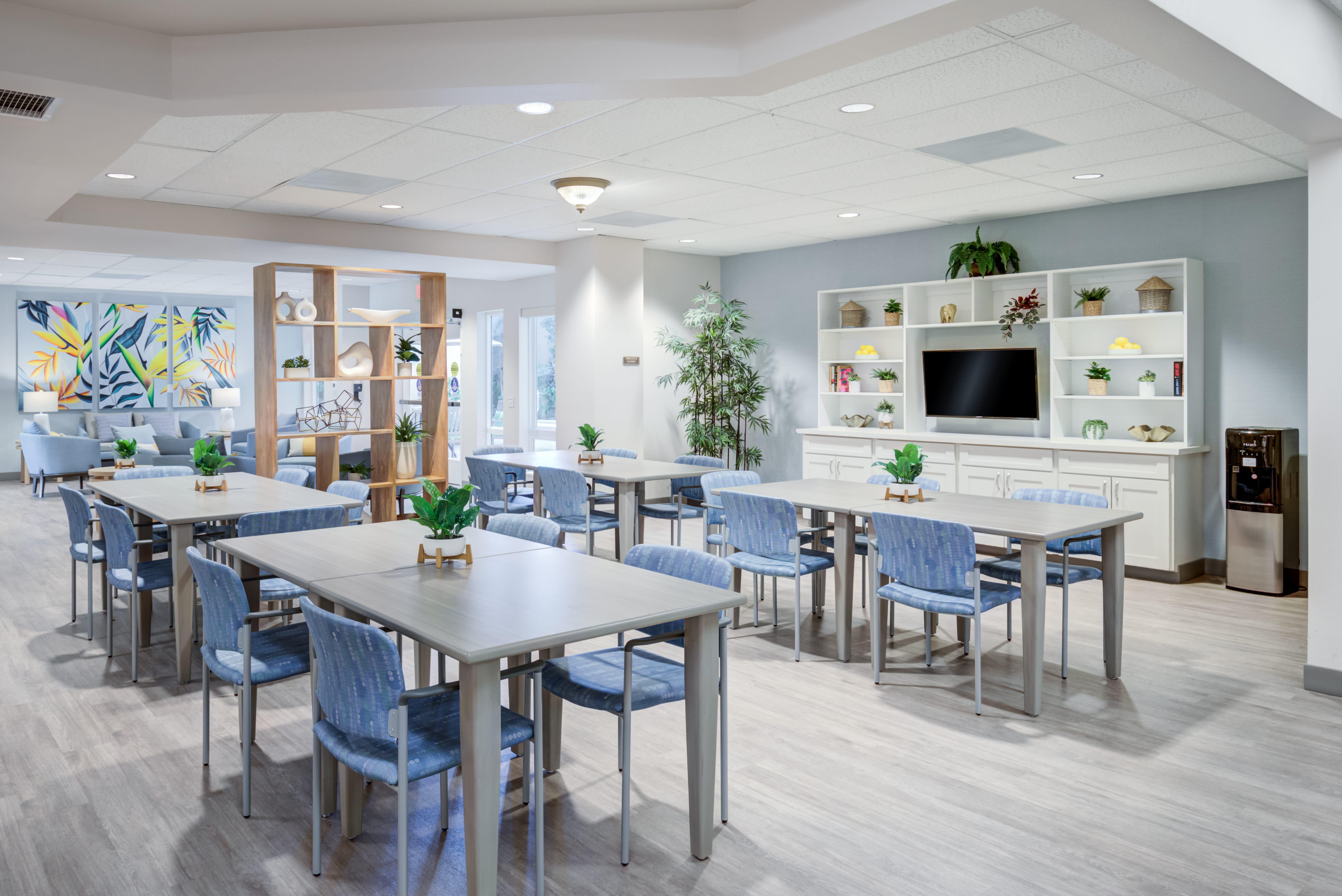 Group activity room with gray tables and blue chairs at a local senior living home.
