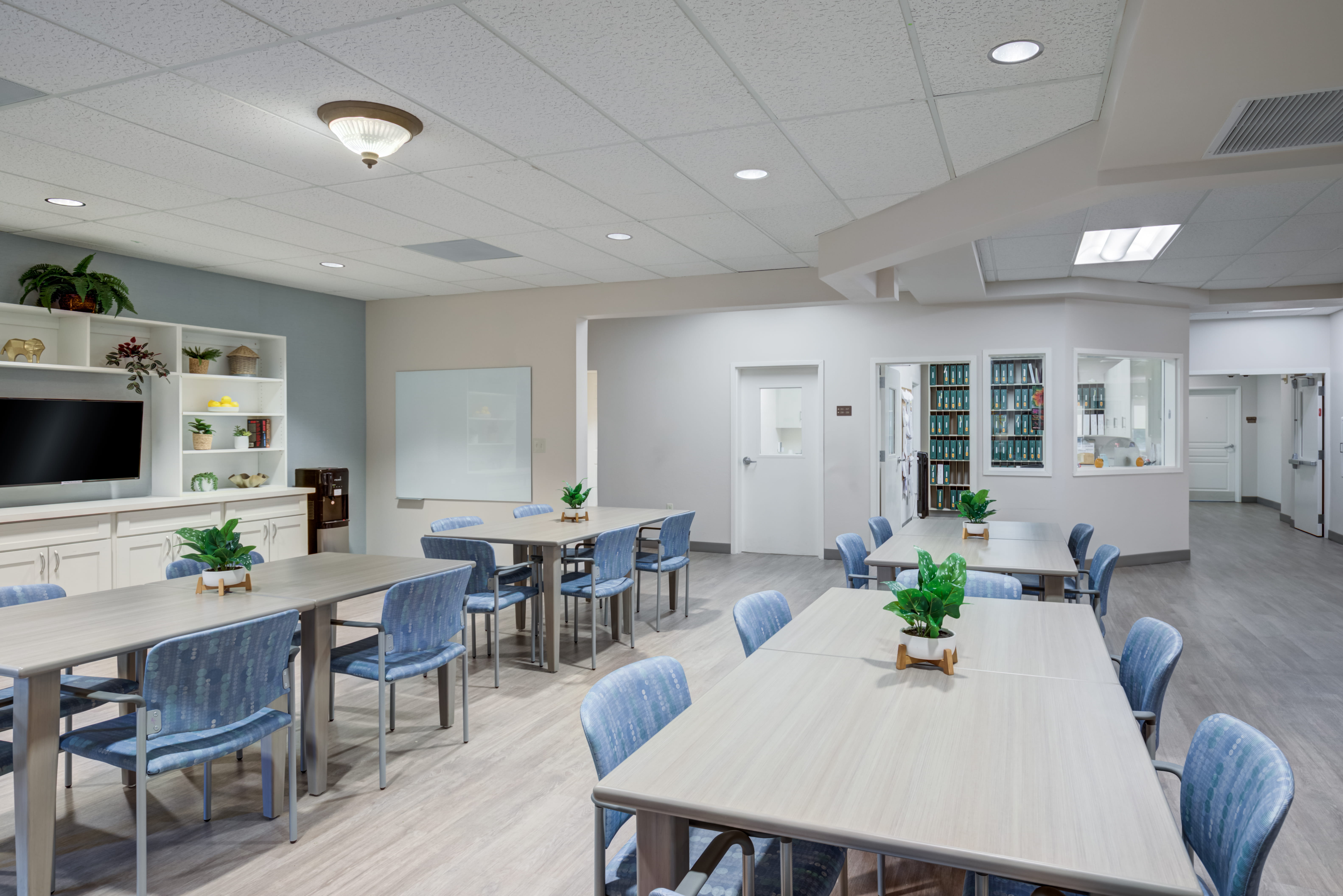 Activity room with tables, blue chairs, and a TV at an assisted living facility.