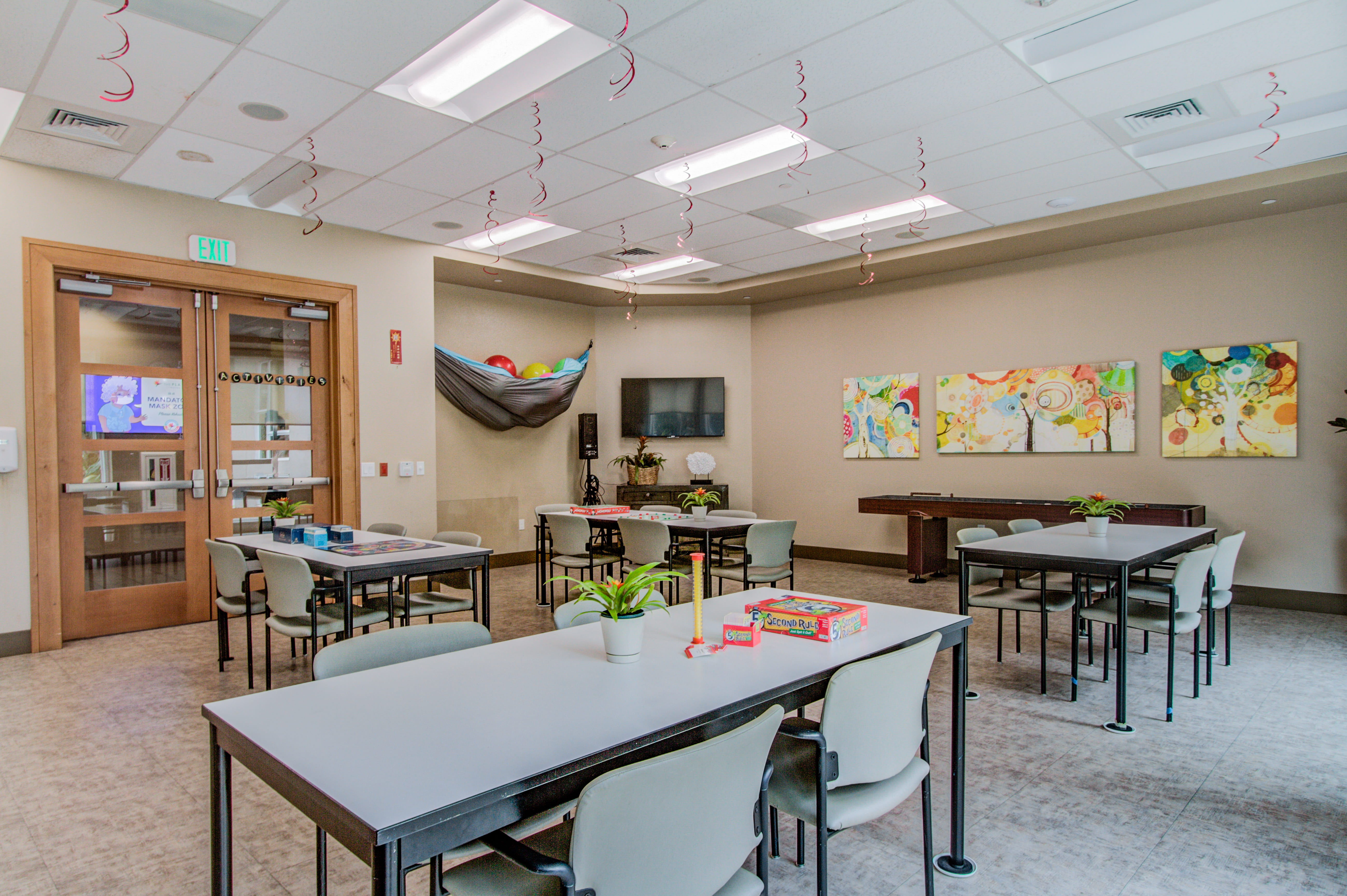 Activity room with white tables and festive streamers at The Plaza Assisted Living.
