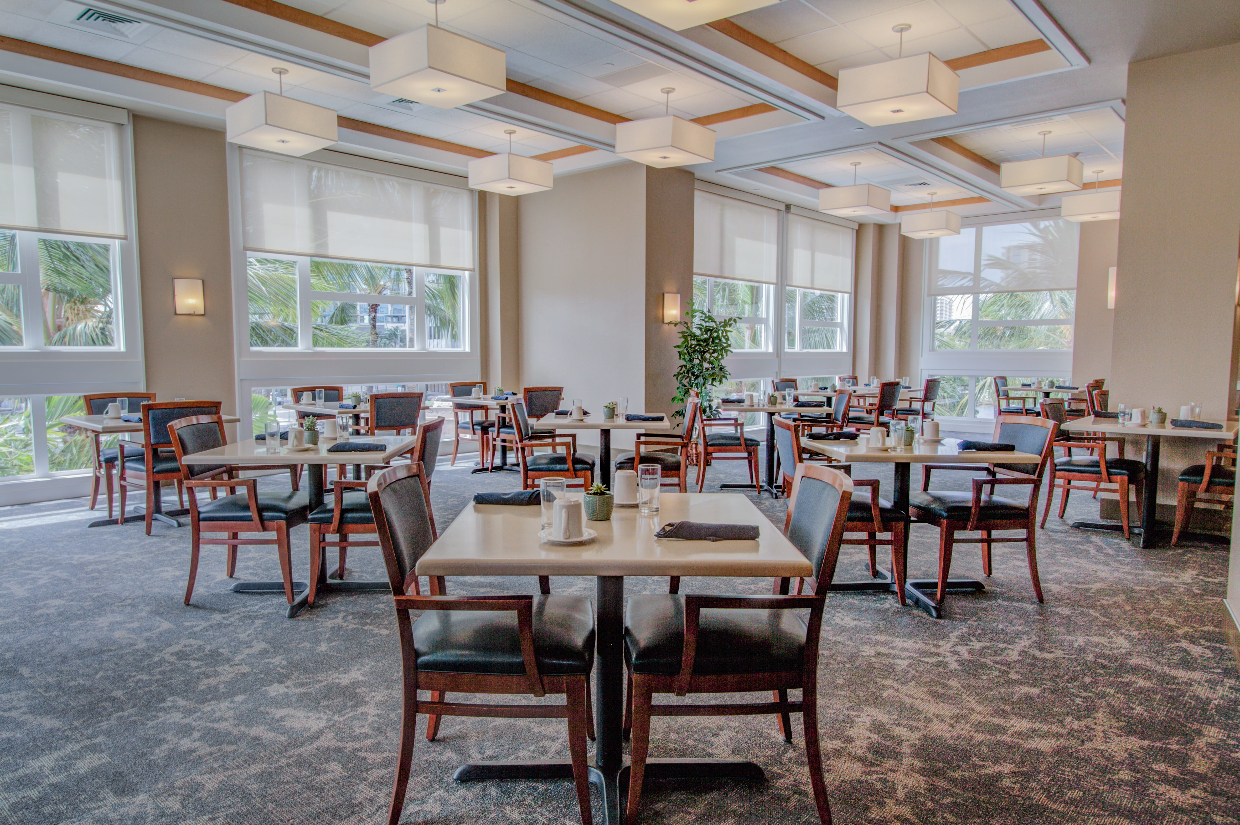 Spacious dining hall with square light fixtures and views of palm trees.