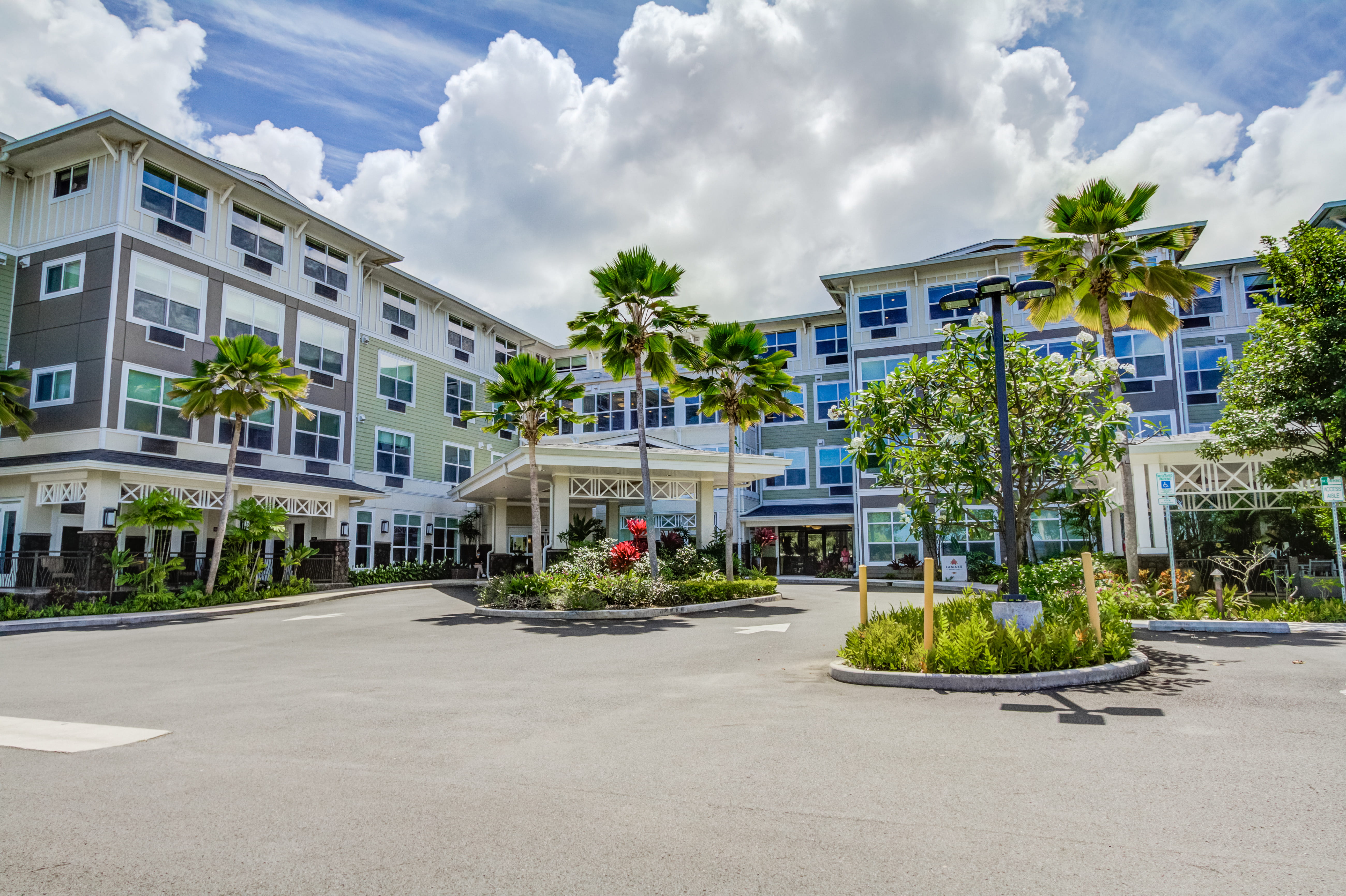 Exterior view of The Plaza Assisted Living facility and palm-lined driveway.