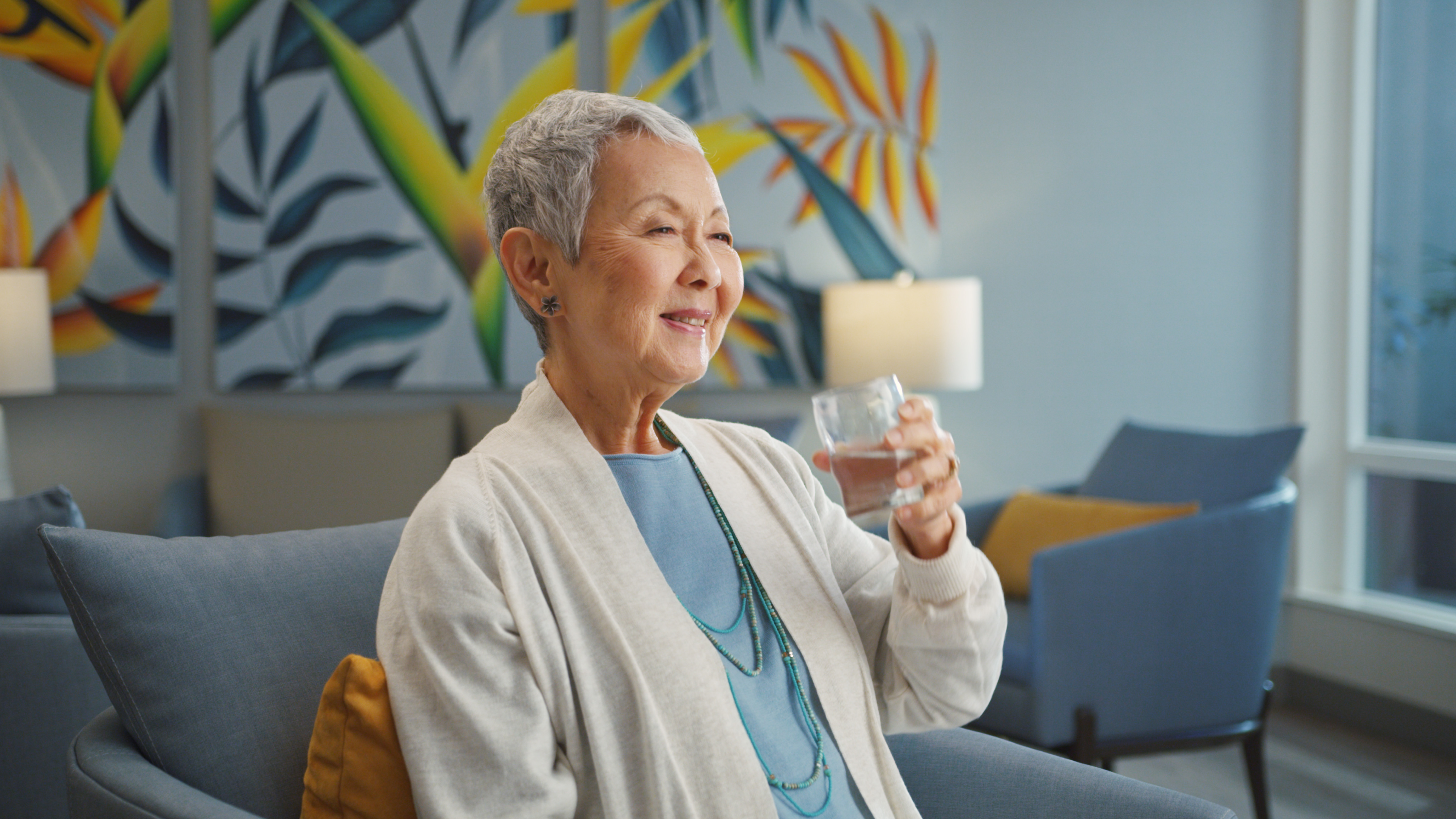 Senior woman smiling while holding a glass of water at The Plaza Assisted Living.